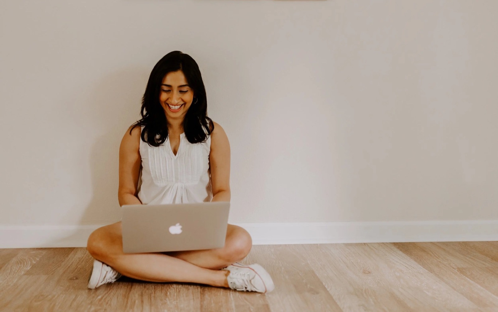 Arundhati seated on the floor against a pale wall, smiling at an open laptop during an online teaching session.