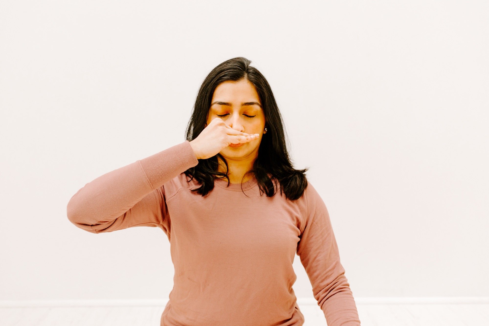 A student seated upright with eyes closed, fingers in nasikagra mudra closing one nostril during alternate-nostril breathing.