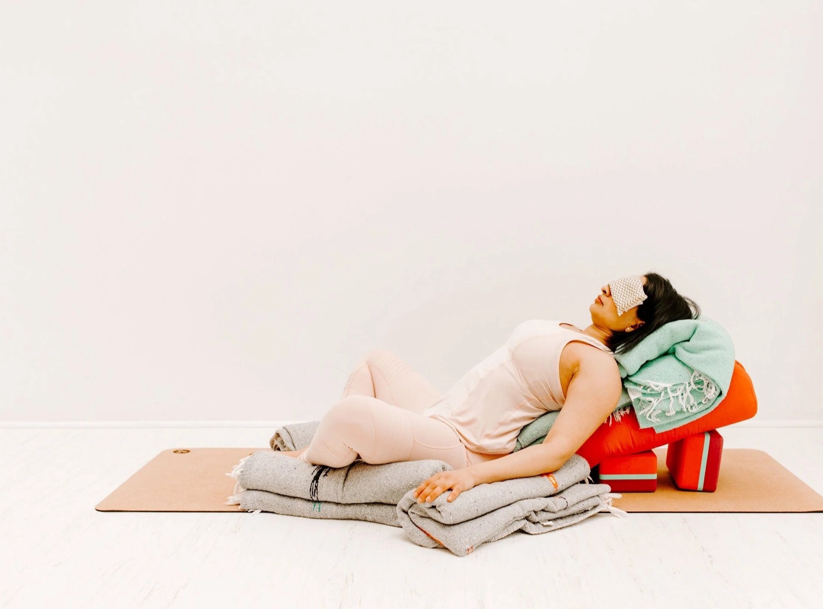 A student resting in supported reclined bound angle pose, eyes covered, supported by a bolster, blocks, and folded blankets.