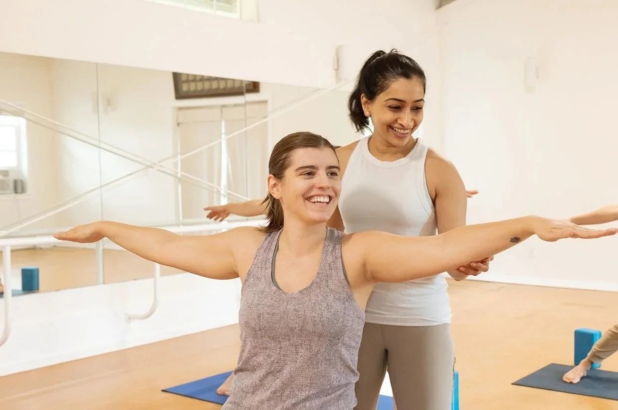 A teacher guiding a smiling student's arms into position during a hands-on adjustment in the Redmond studio.